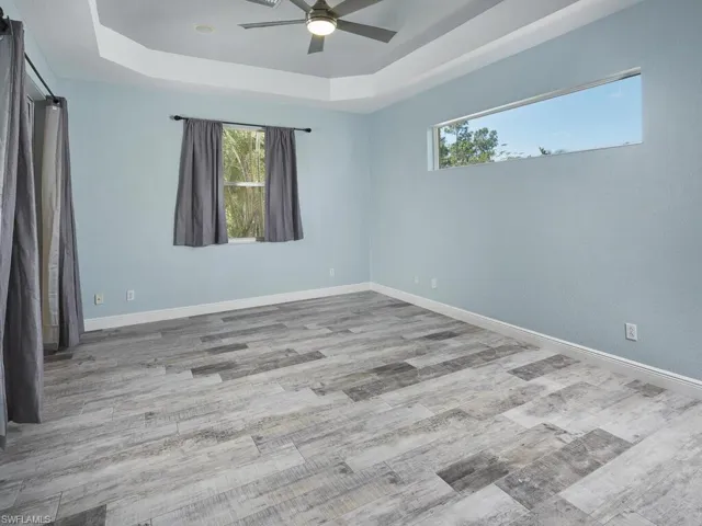 Peaceful primary bedroom with tray ceiling, large windows, and updated flooring.