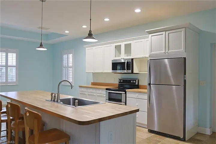 Kitchen featuring stainless steel appliances, glass insert cabinets, hanging light fixtures, white cabinetry, and a kitchen island with sink