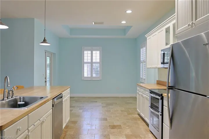 Kitchen featuring stainless steel appliances, a raised ceiling, hanging light fixtures, wood counters, and light stone finish flooring