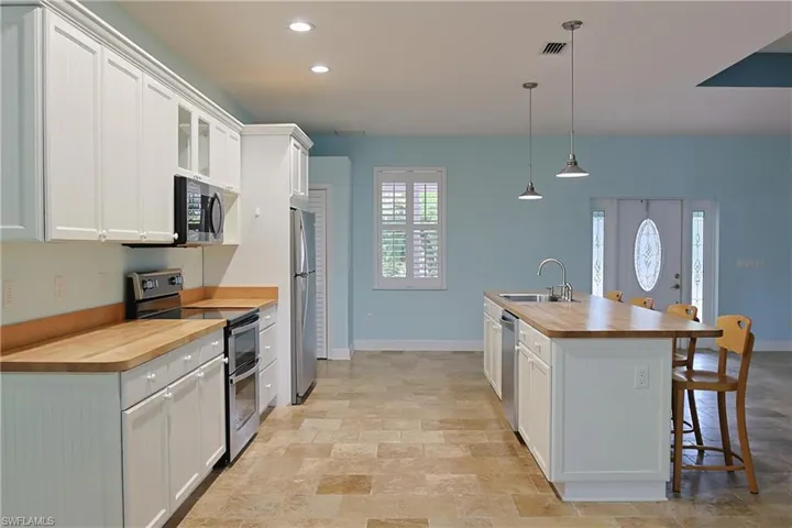 Kitchen featuring wood counters, stainless steel appliances, white cabinetry, a breakfast bar, and stone finish floors