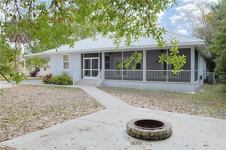 View of front of property with a fire pit, a metal roof, a carport, and a sunroom
