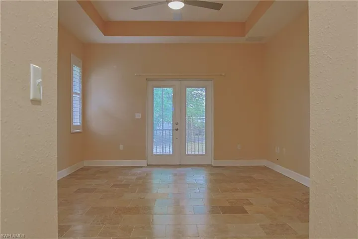 Unfurnished room featuring a textured wall, french doors, ceiling fan, healthy amount of natural light, and a raised ceiling