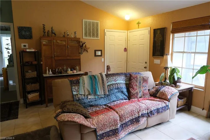 Living area featuring vaulted ceilings, tile flooring, a large window with natural light, and two panel doors