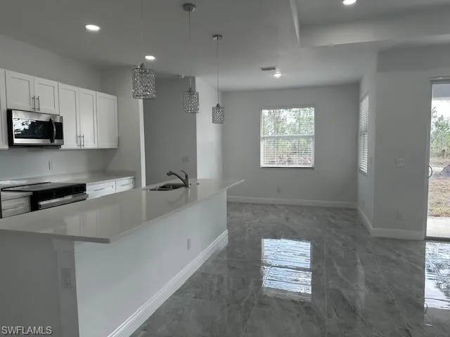 Kitchen with sink, white cabinets, a kitchen island with sink, and decorative light fixtures