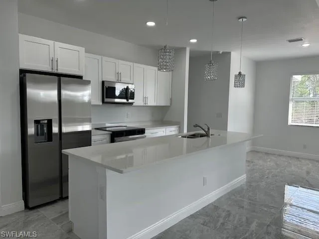 Kitchen with hanging light fixtures, appliances with stainless steel finishes, sink, and white cabinets