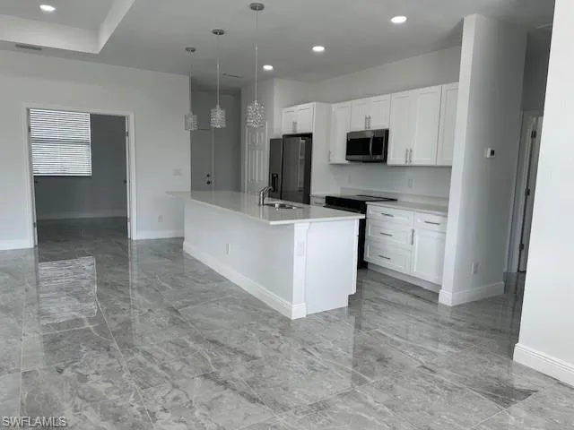 Kitchen with a kitchen island with sink, black appliances, sink, white cabinets, and pendant lighting