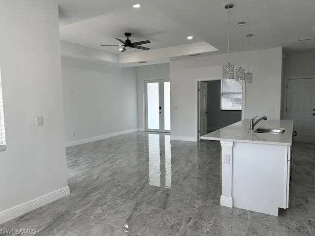 Kitchen with an island with sink, hanging light fixtures, sink, a tray ceiling, and ceiling fan