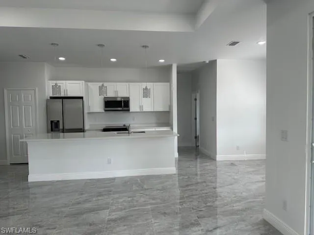 Kitchen featuring a center island with sink, hanging light fixtures, white cabinetry, and stainless steel appliances