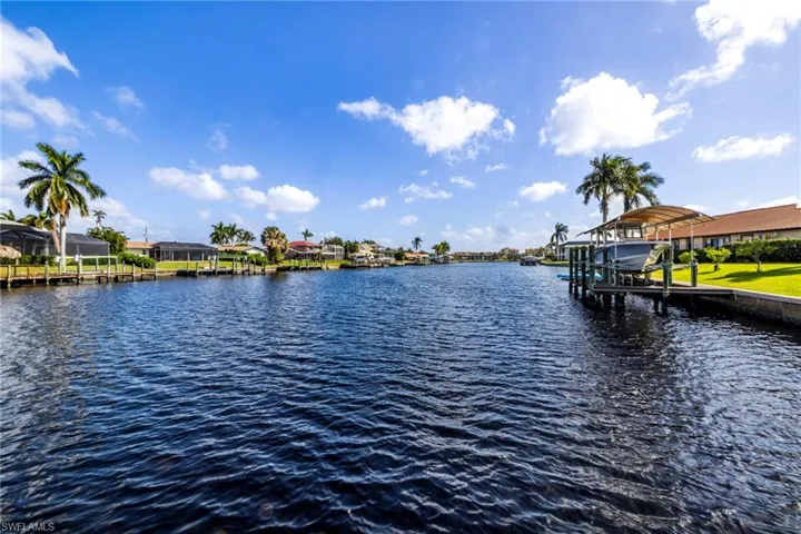 Waterfront property featuring a canal-side boat dock with a covered canopy, manicured lawn, and mature palm trees