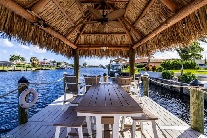 Waterfront dock featuring a thatched-roof tiki structure, composite deck surface, integrated ceiling fan, and wooden mooring pilings