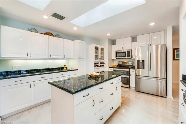 Kitchen featuring white shaker-style cabinetry, a central island with storage drawers, polished dark stone countertops, stainless steel appliances, and ceiling skylights