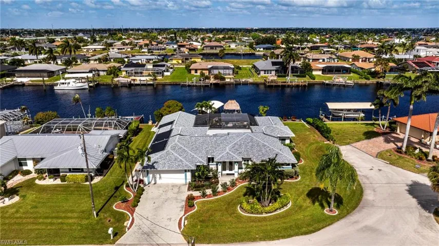 Waterfront property featuring a canal-side bulkhead, a screened-in lanai, and a shingle roof with integrated solar panels
