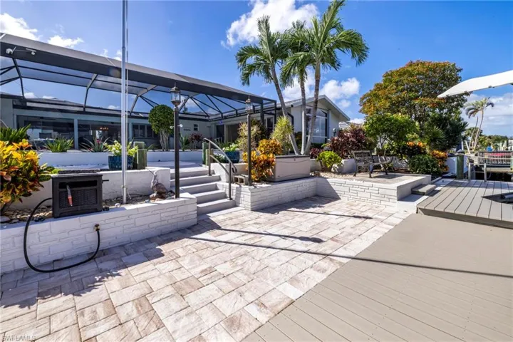 Screened-in outdoor patio featuring tiered stone retaining walls, paver flooring, synthetic decking, and dock access