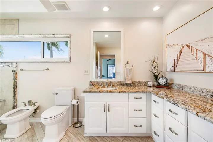 Bathroom featuring an extended vanity with stone-surfaced countertops, white cabinetry with silver-tone hardware, a wall-mounted rectangular mirror, recessed lighting, and tile flooring