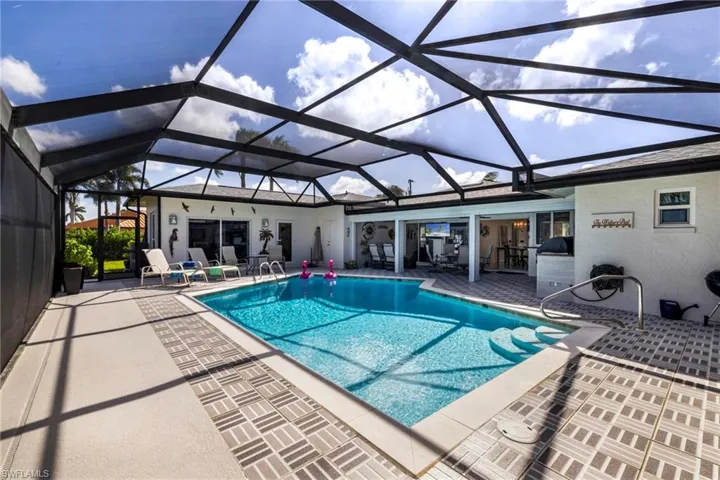 Screened-in outdoor living area featuring an in-ground swimming pool, patterned tile decking, integrated poolside bar, and structural metal enclosure