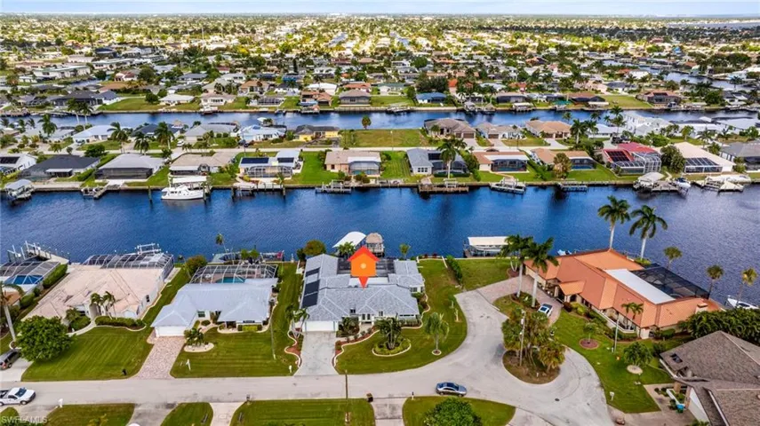 Waterfront property featuring deep-water canal access, private boat dock, tiled roof, paved driveway, and expansive lawn