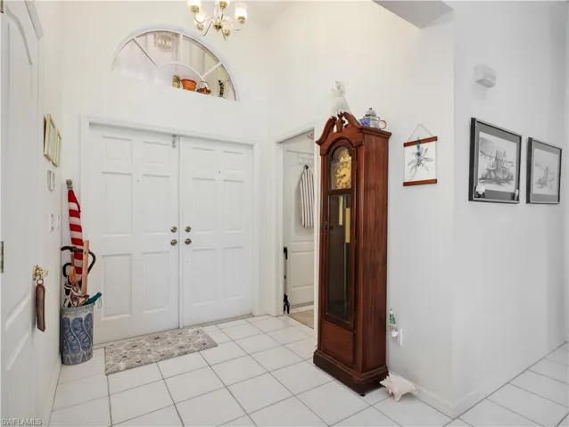 Bright foyer featuring double entry doors with an arched transom window, a chandelier, and white tile flooring