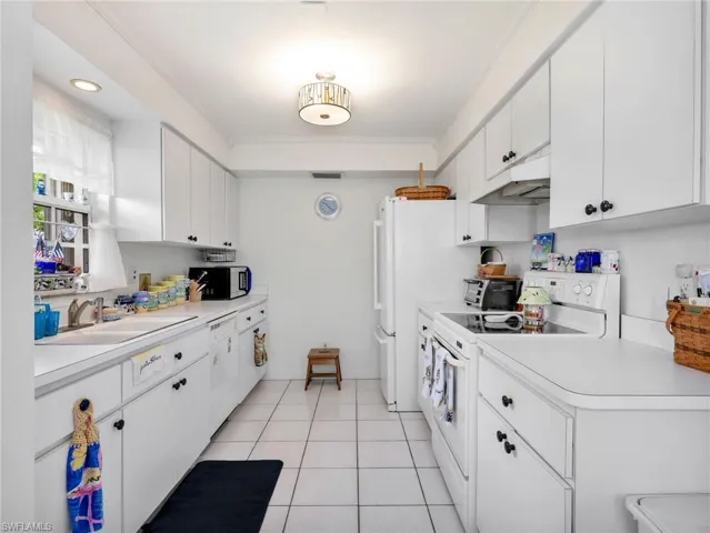 Galley kitchen featuring white cabinetry with black hardware, white appliances, white countertops, and white square tile flooring