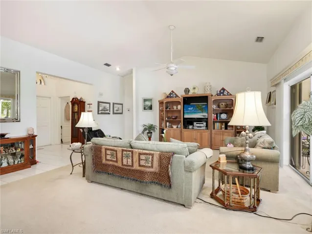 Vaulted ceilings define this living area, featuring light-toned carpeting and direct access to an outdoor space via sliding glass doors