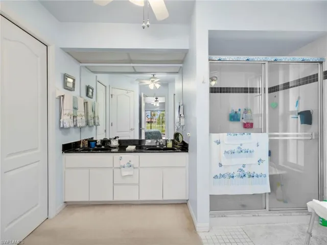 Main Bathroom featuring a dual vanity with a dark countertop and undermount sinks, a large mirror, a glass-enclosed shower with tile surround, and a ceiling fan