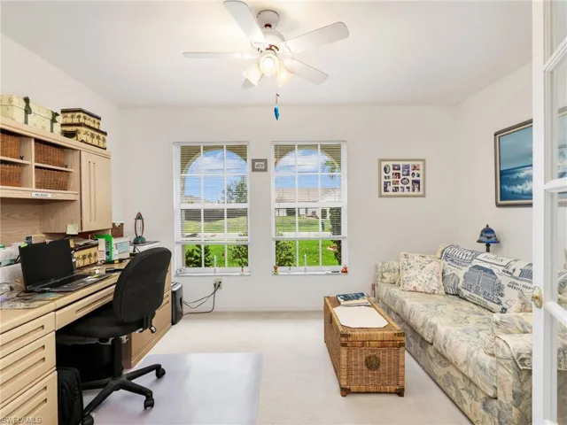 Light-filled interior space featuring two arched windows, a ceiling fan with integrated lighting, and carpeted flooring