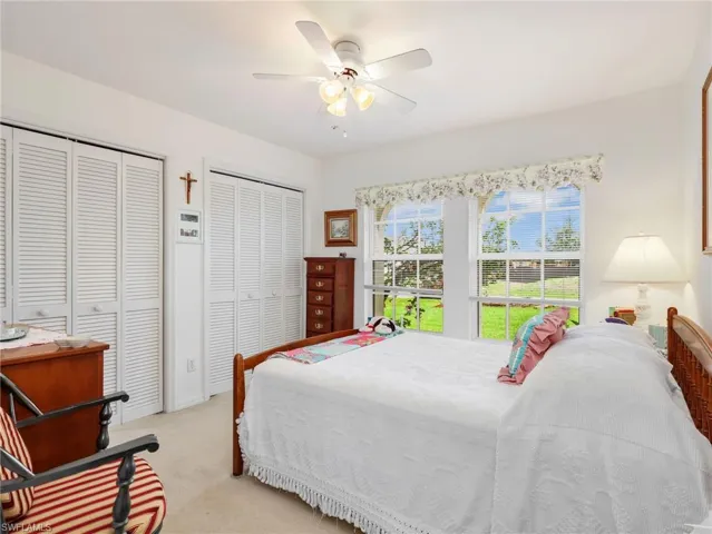 Bright interior featuring a ceiling fan, dual shuttered closets, and two large arched windows overlooking a green landscape