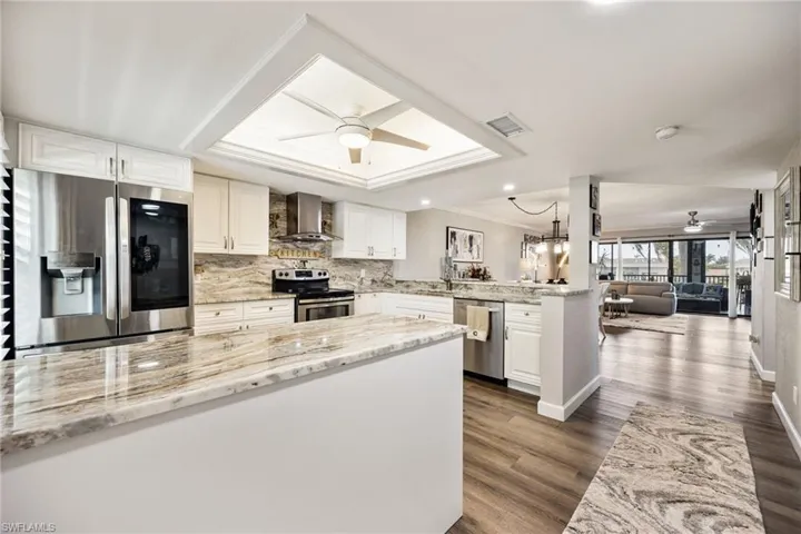 Open-concept kitchen featuring extensive stone countertops, white cabinetry, stainless steel appliances, and wood-finish flooring