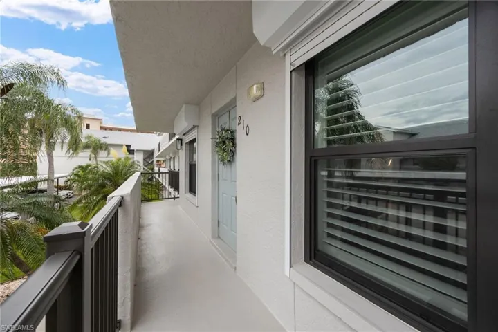 Exterior corridor featuring a light blue entry door with decorative wreath, exterior lighting, window with horizontal blinds, and a durable metal railing