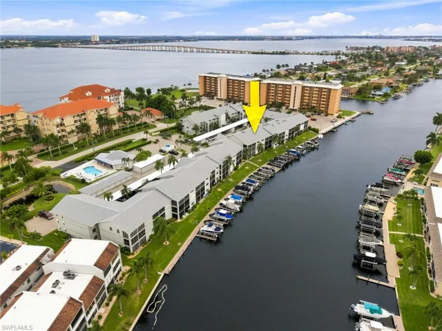 Waterfront condominium building featuring private boat slips, direct canal access, a community pool, and a large body of water in the background