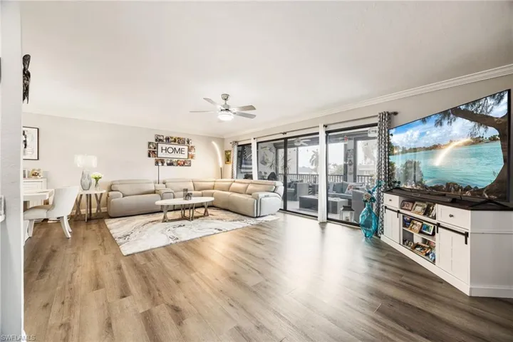 Spacious living area featuring wood-finish flooring, a ceiling fan, and sliding glass doors opening to an outdoor screened area