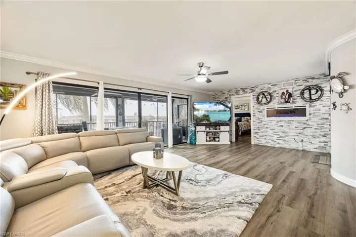 Spacious living area featuring wood-finish flooring, a ceiling fan, and crown molding