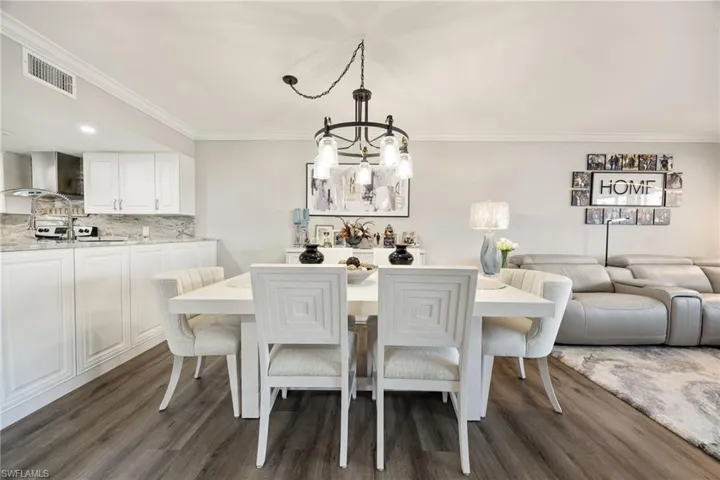 Open-concept dining area featuring wood-finish flooring, crown molding, and a contemporary chandelier