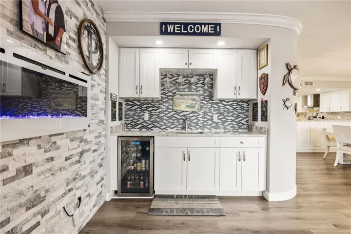 Wet bar featuring white shaker cabinetry, patterned tile backsplash, granite-style countertop, and a built-in beverage refrigerator