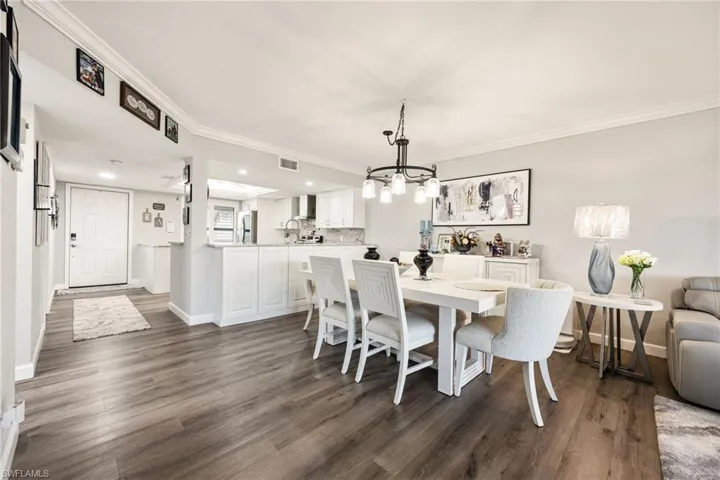 Open-concept living area featuring wood-finish flooring, crown molding, and a contemporary chandelier