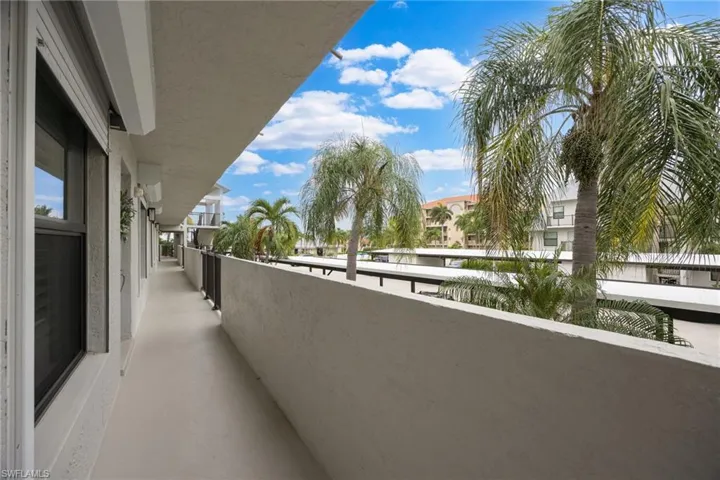 Exterior balcony featuring a smooth concrete floor, textured stucco walls, and a dark metal railing