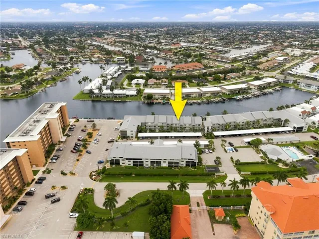 Aerial view of a multi-building property featuring waterside positioning, multiple boat docks, a swimming pool, and extensive parking facilities