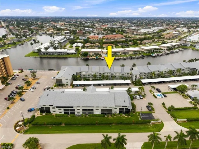 Waterfront condominium building featuring multiple units, covered parking, and an expansive paved parking area