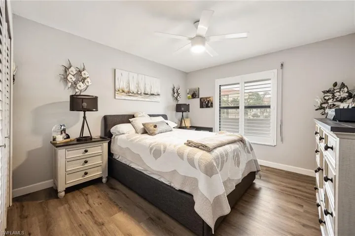 Bedroom featuring wood-finish flooring, a ceiling fan with integrated lighting, and a window with plantation shutters