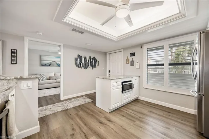 Open-concept kitchen with wood-finish flooring, white cabinetry, integrated microwave, and a tray ceiling with a ceiling fan