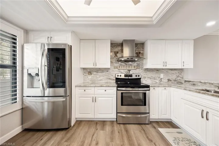 Kitchen featuring white cabinetry, light-toned granite countertops, stainless steel appliances, and wood-finish flooring