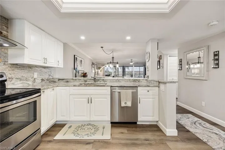 Well-appointed kitchen featuring white cabinetry, stainless steel appliances, a light-toned stone countertop, a matching stone backsplash, and wood-finish flooring