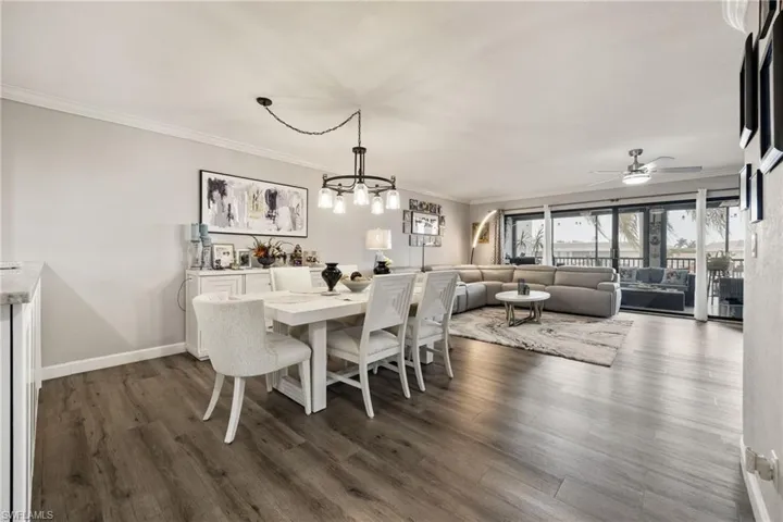 Open-concept living space with wood-finish flooring, crown molding, and a contemporary dining area chandelier