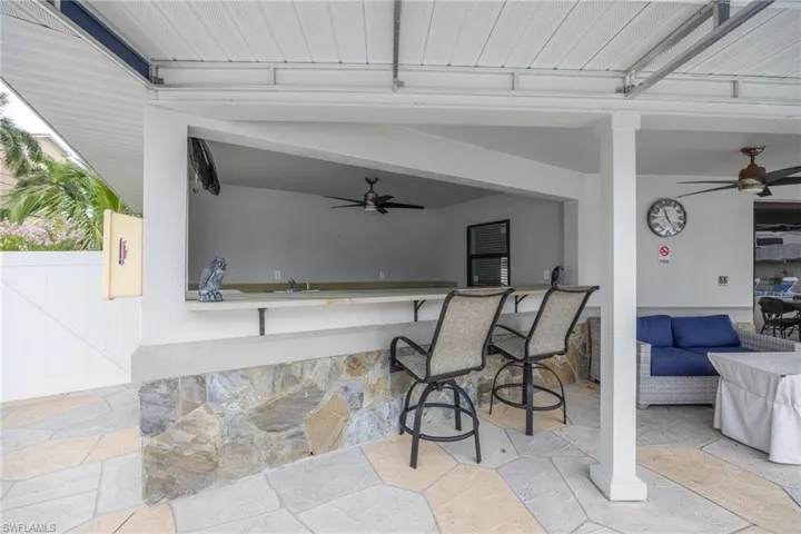 Covered patio featuring an outdoor bar area with stone-finish base, ample counter space, and integrated ceiling fans