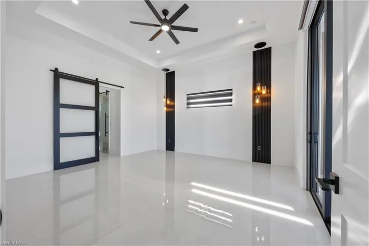 Empty room with a barn door, a raised ceiling, recessed lighting, and a ceiling fan