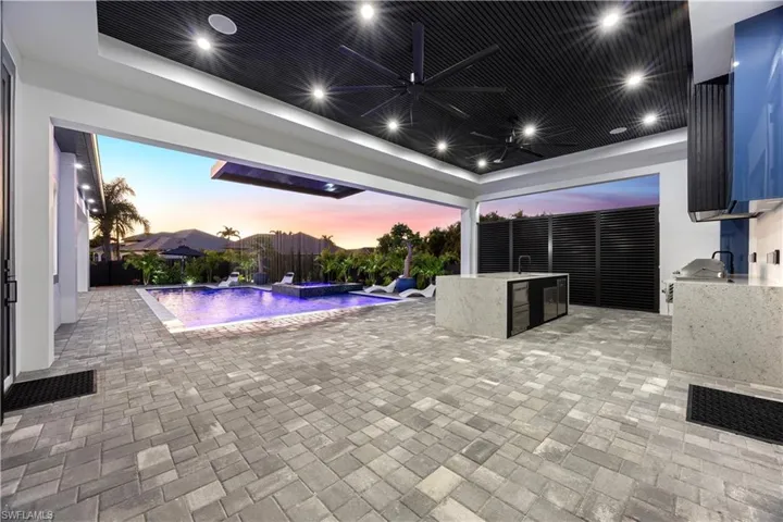 Fenced backyard featuring an outdoor kitchen, a patio area, a pool with connected hot tub, and ceiling fan