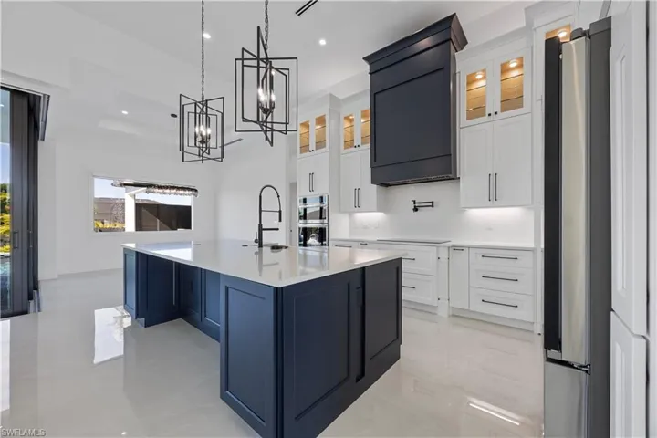 Kitchen with white cabinets, glass insert cabinets, hanging light fixtures, a kitchen island with sink, and appliances with stainless steel finishes