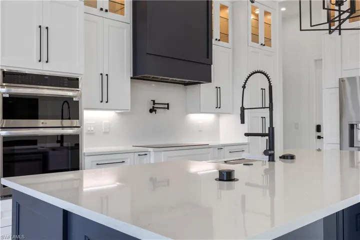Kitchen with stainless steel appliances, white cabinets, glass insert cabinets, and light stone counters