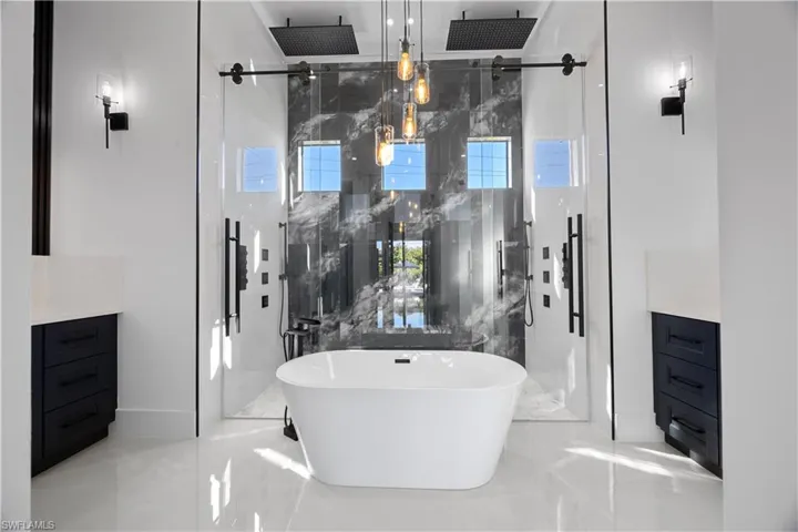 Bathroom with vanity, a freestanding bath, a marble finish shower, and light marble finish flooring