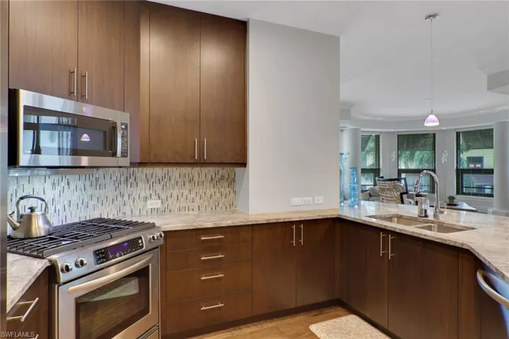 Kitchen with stainless steel appliances, hanging light fixtures, light stone countertops, light wood finished floors, and modern cabinets