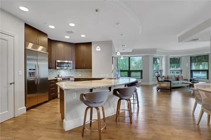 Kitchen featuring stainless steel appliances, pendant lighting, light stone countertops, open floor plan, and a breakfast bar